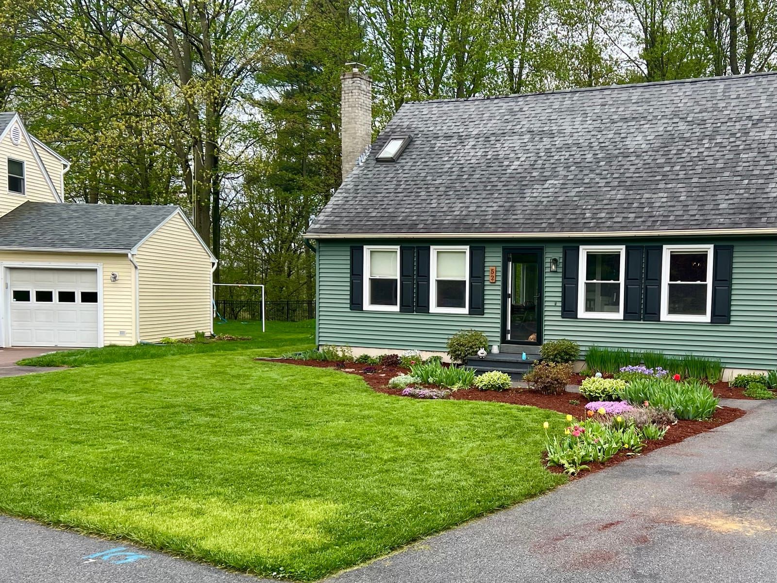 A green front lawn and flower beds in front of a Cape house