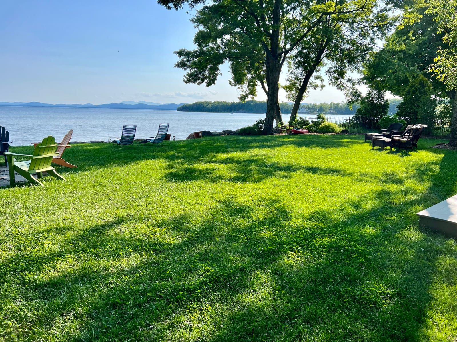 A lakeside lawn with Adirondack chairs by the water