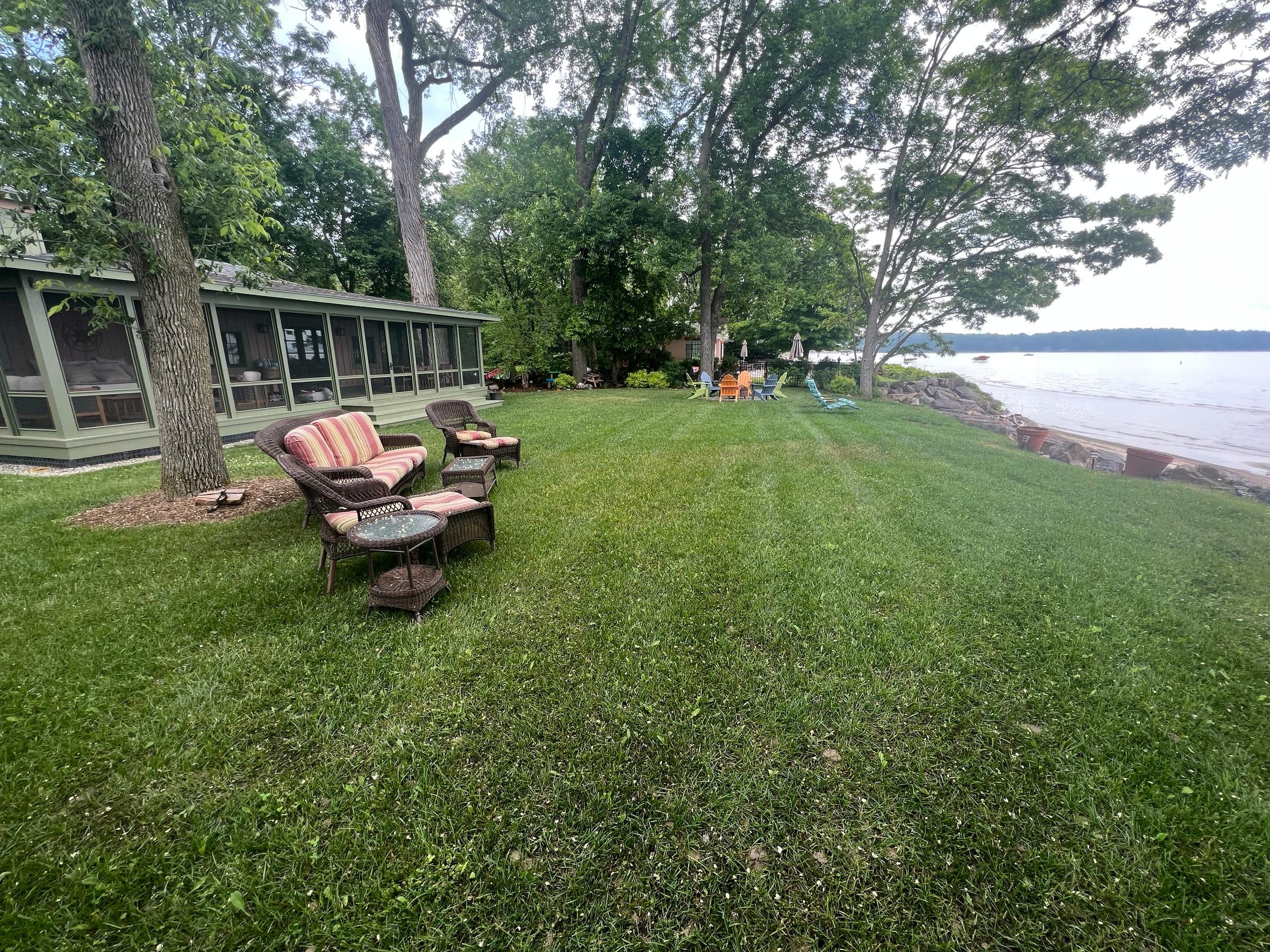 Patio chairs and a fire pit on a green lakeside lawn