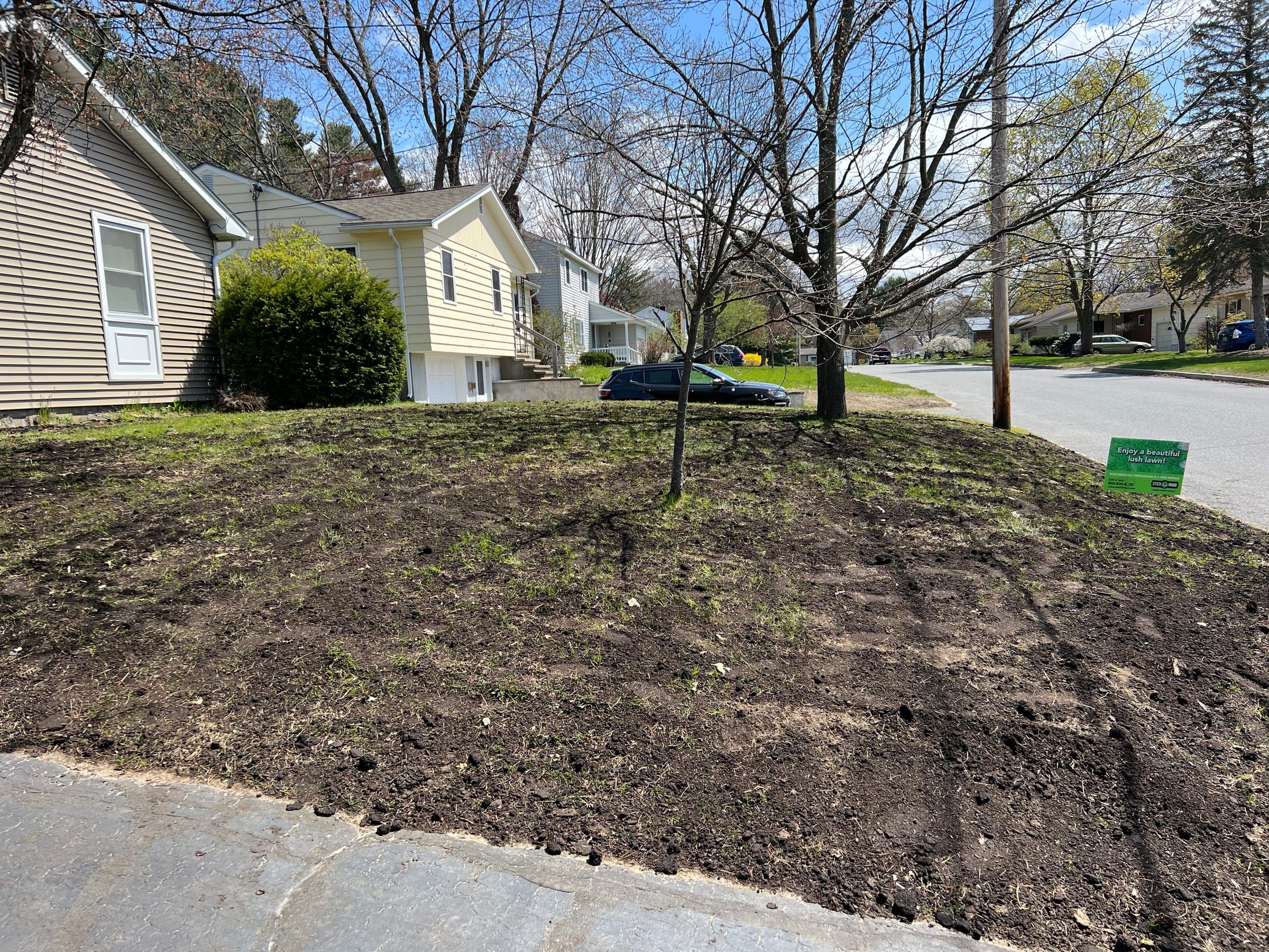 A front-yard slope freshly seeded, with the Stick2Mud sign on the lawn