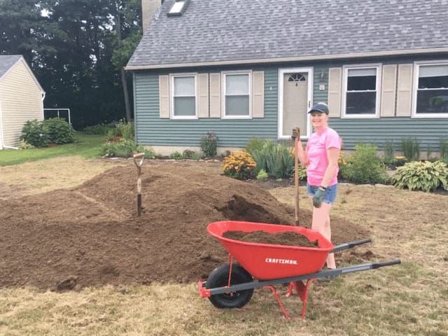Topsoil piled on a front yard with a wheelbarrow, ready to spread